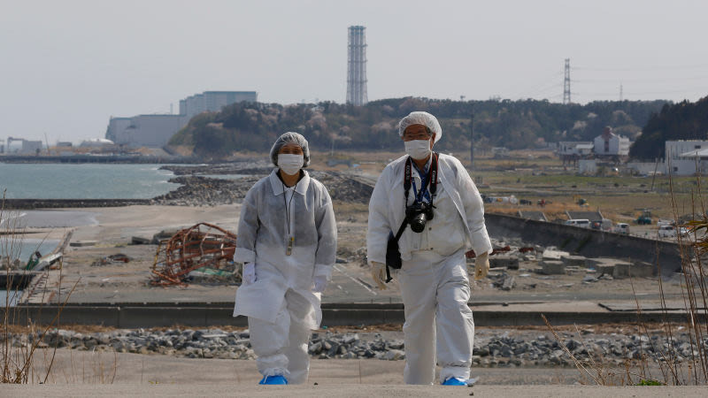 Una pareja camina por las costas cercanas a la devastada central de Fukushima, usando ropa protectora. AP